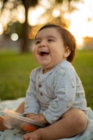 A baby laughing joyfully while sitting inside a decorated cardboard box with soft toys.