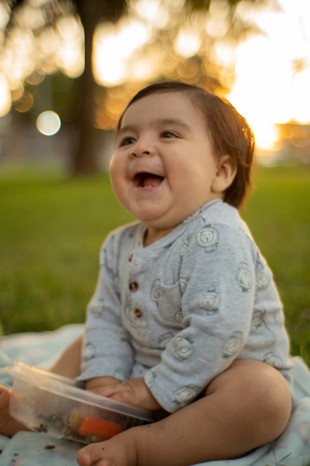 A joyful baby laughing while sitting on a soft blanket with colorful toys