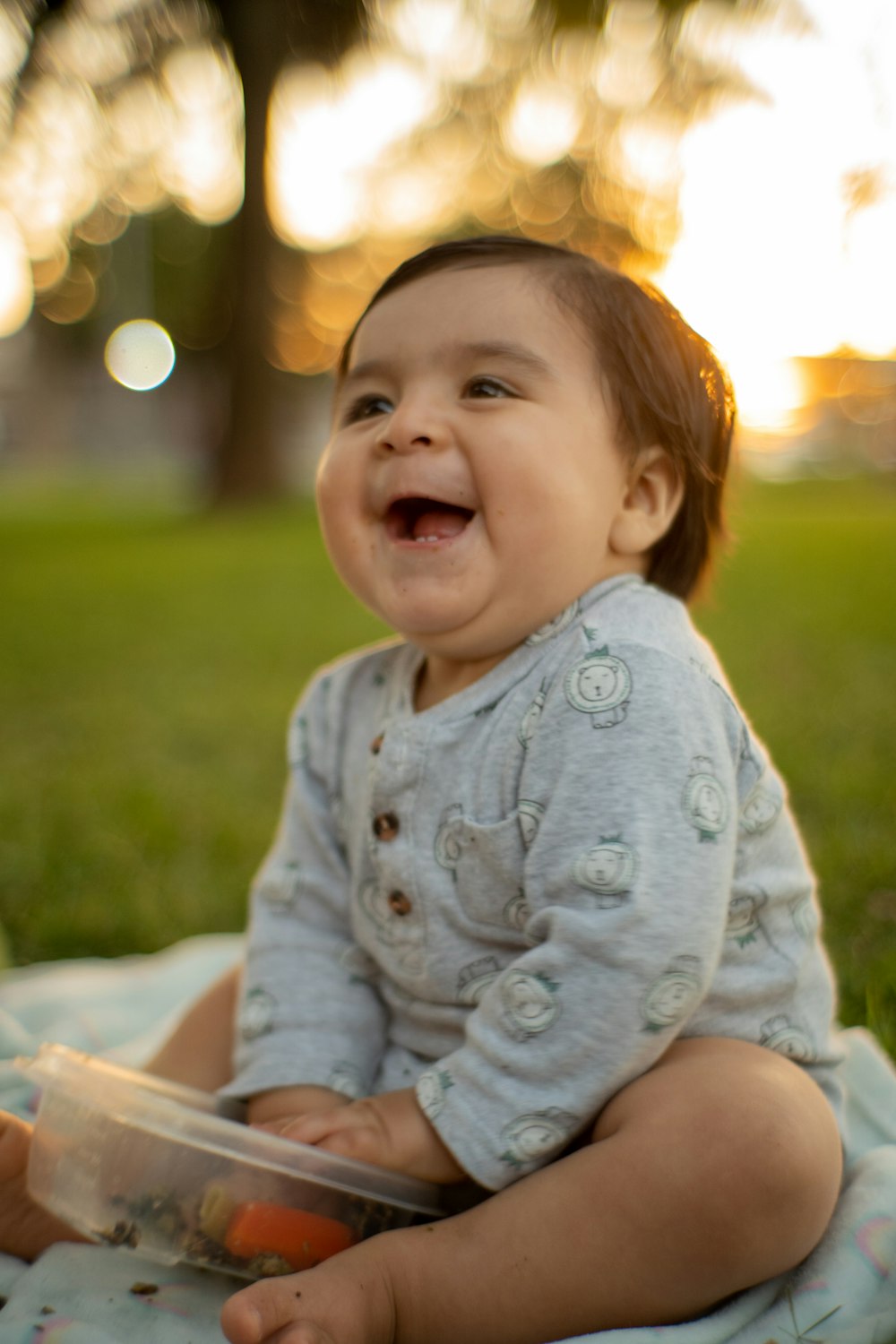 a smiling baby sitting on a blanket in the grass