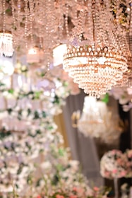 A lavish and ornate chandelier made of crystals hanging from the ceiling. Surrounding the chandelier are numerous decorative elements, including strings of crystals and floral arrangements. The lighting is warm and creates a luxurious ambiance.