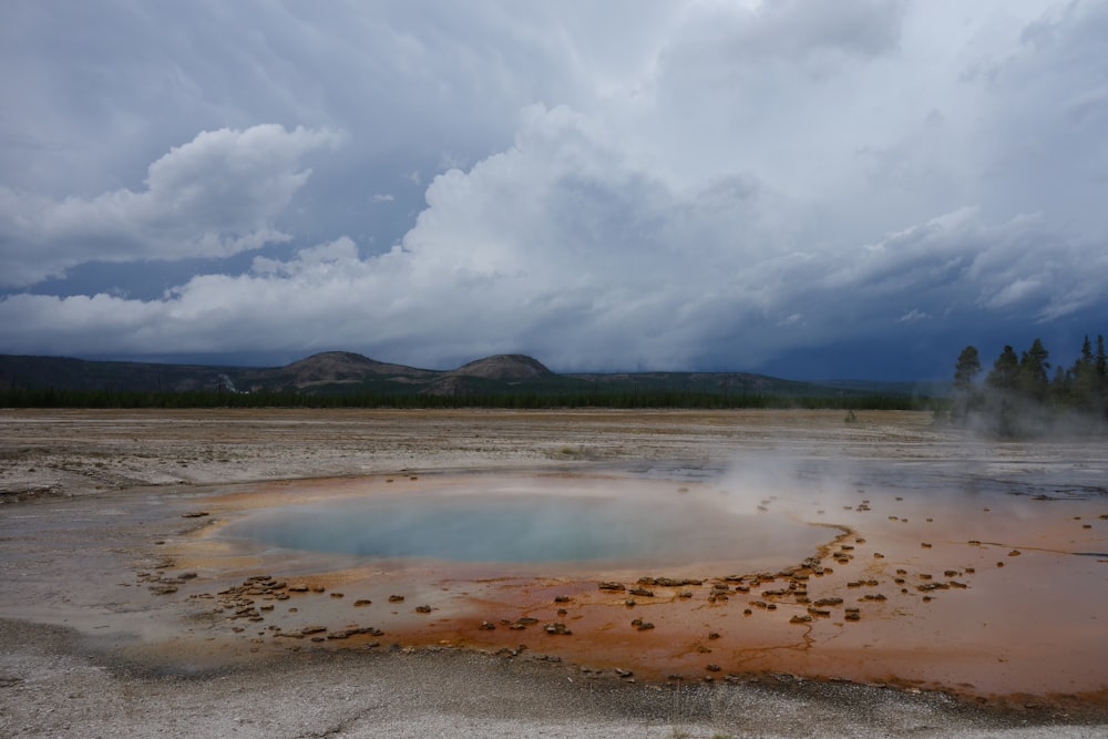 a large pool of water surrounded by rocks under a cloudy sky