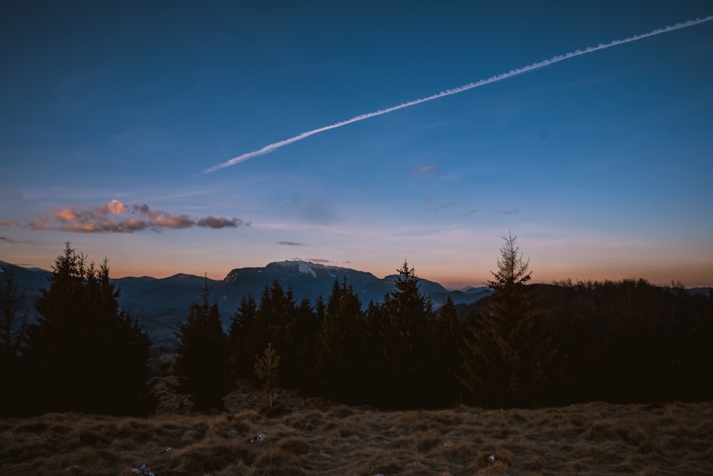 a view of a mountain range at sunset with a contrail in the sky