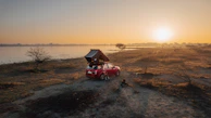 A family enjoying breakfast beside their car with a rooftop tent set up in a sunny meadow.