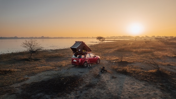A cozy car interior at sunset with a wildrise air mattress set up, surrounded by forest scenery.