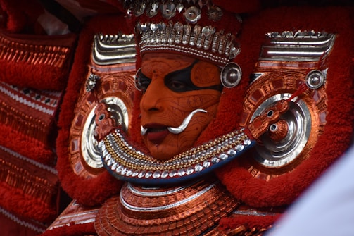 A traditional performer adorned with elaborate face paint and intricate costume elements. The vibrant colors and metallic embellishments highlight a cultural or ritual aspect.
