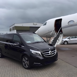 A sleek black luxury van waiting at Santorini airport with a professional chauffeur holding a welcome sign.