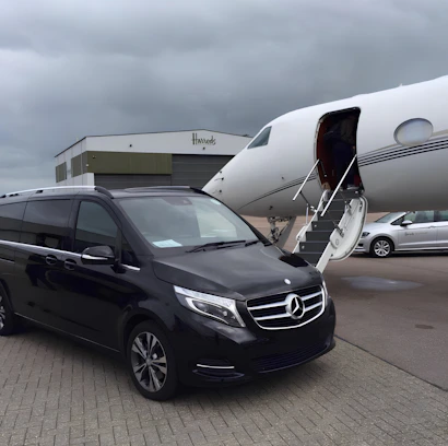 A sleek black Maybach Vito van parked in front of a modern airport terminal at dusk.