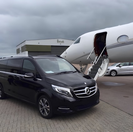 A comfortable black car parked outside a London airport terminal with a smiling driver ready to assist passengers.