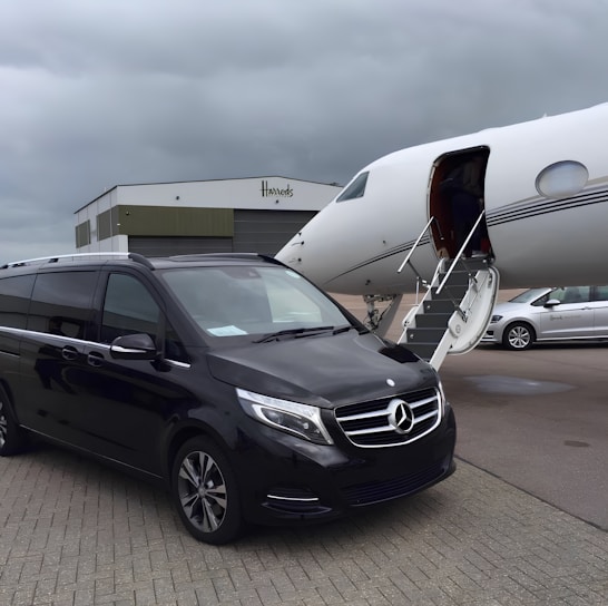 A sleek black car parked outside Heathrow Airport with the Handsome Transport logo visible on the door.