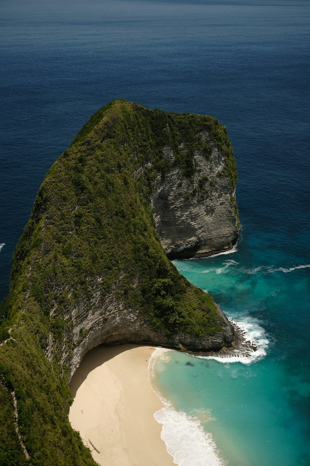 an aerial view of a beach with a large rock sticking out of the water
