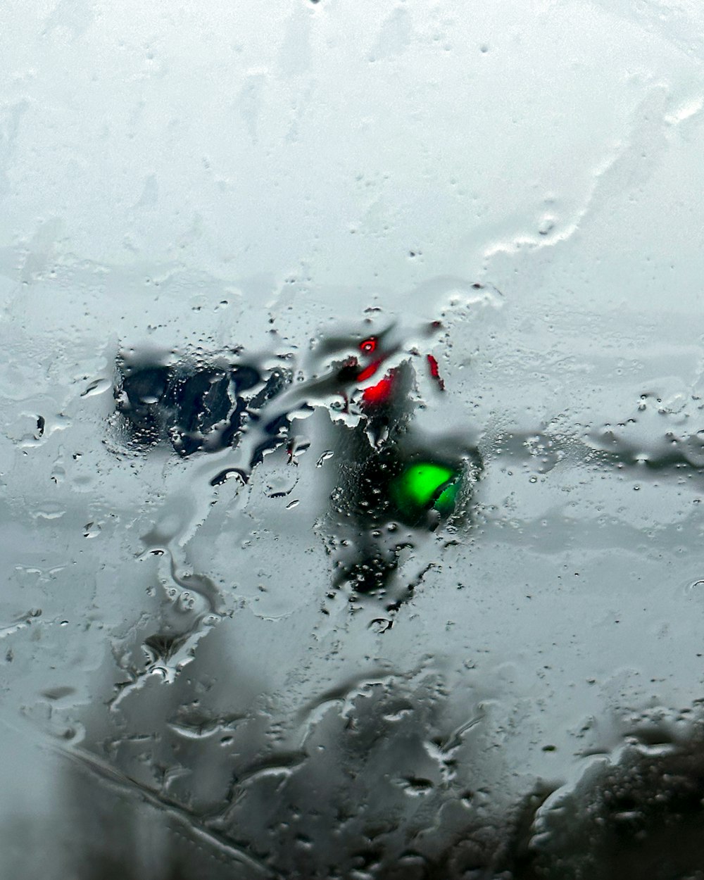 una vista di un semaforo attraverso un parabrezza coperto di pioggia