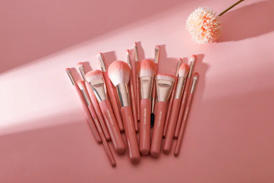 A collection of elegant makeup brushes and accessories laid out on a soft pink fabric.