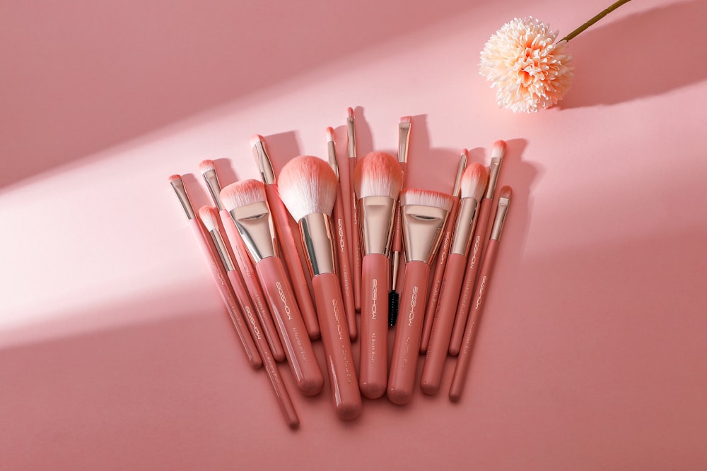 a bunch of makeup brushes sitting on top of a pink surface