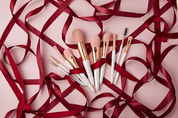 Elegant bridal makeup brushes and mehndi cones arranged on a soft white fabric with gold accents.