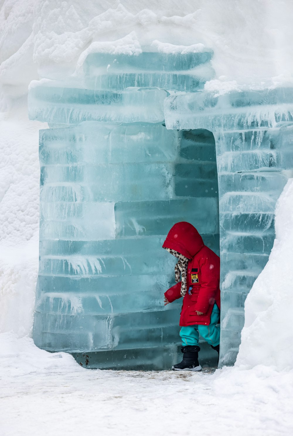 a person in a red jacket and blue pants standing in an ice cave