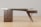 A modern wooden desk with a unique, artistic design features three drawers on the left side and one on the right. The structure includes elegant curves and a glass top. The desk is set against a simple, light-colored background on a wooden floor.