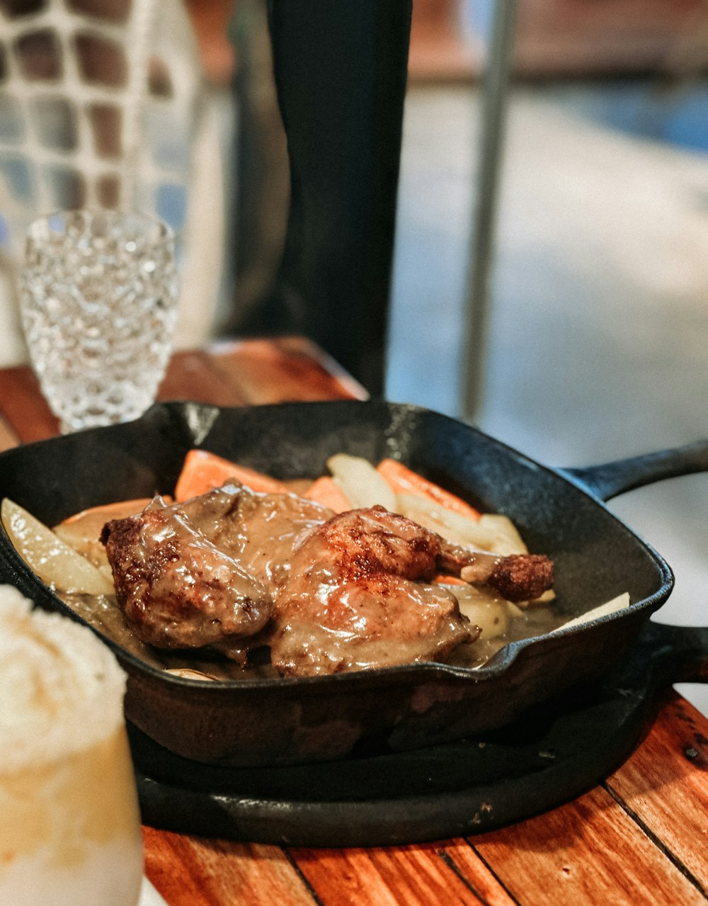 a skillet filled with meat and potatoes on a wooden table