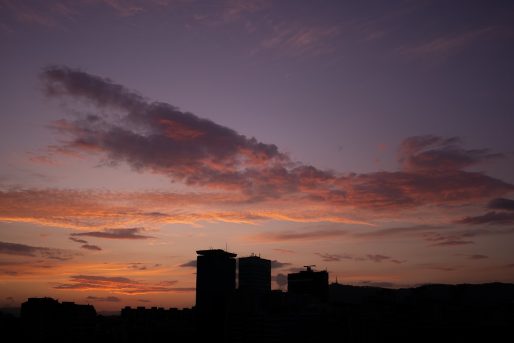 a sunset with clouds and buildings in the background