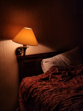 A serene bedroom bathed in soft red light from a modern therapy lamp.