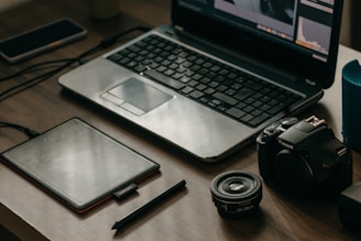 A vibrant workspace featuring a laptop, camera, and design tools on a wooden table.