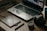 A wooden table with a laptop displaying photo editing software, alongside a graphics tablet, pen, DSLR camera, camera lens, and a smartphone.