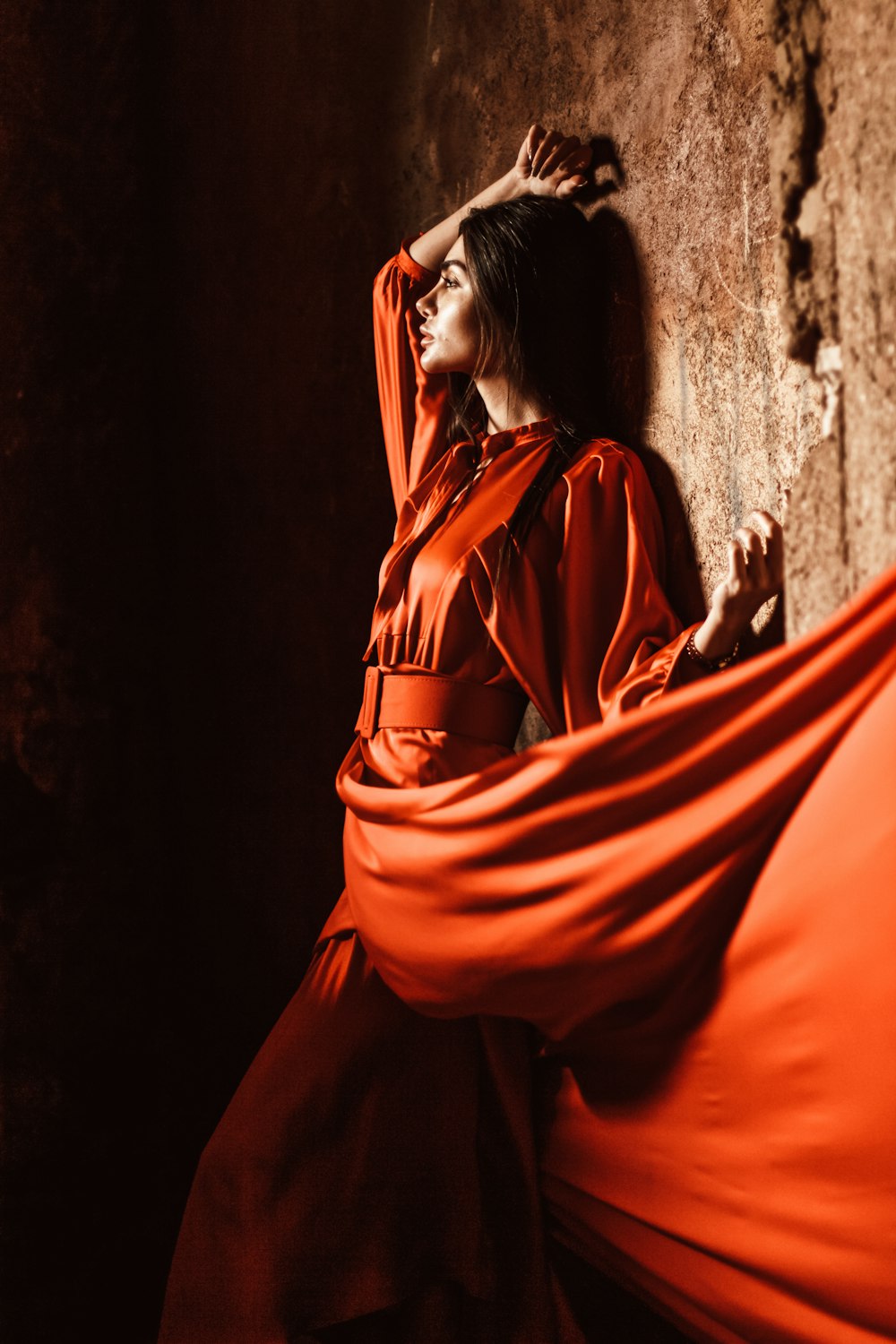 a woman in a red dress leaning against a wall