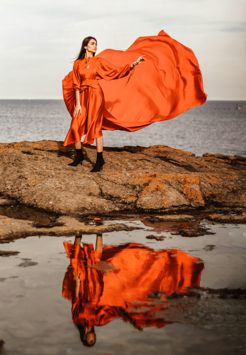 a woman in an orange dress is standing on a rock by the water