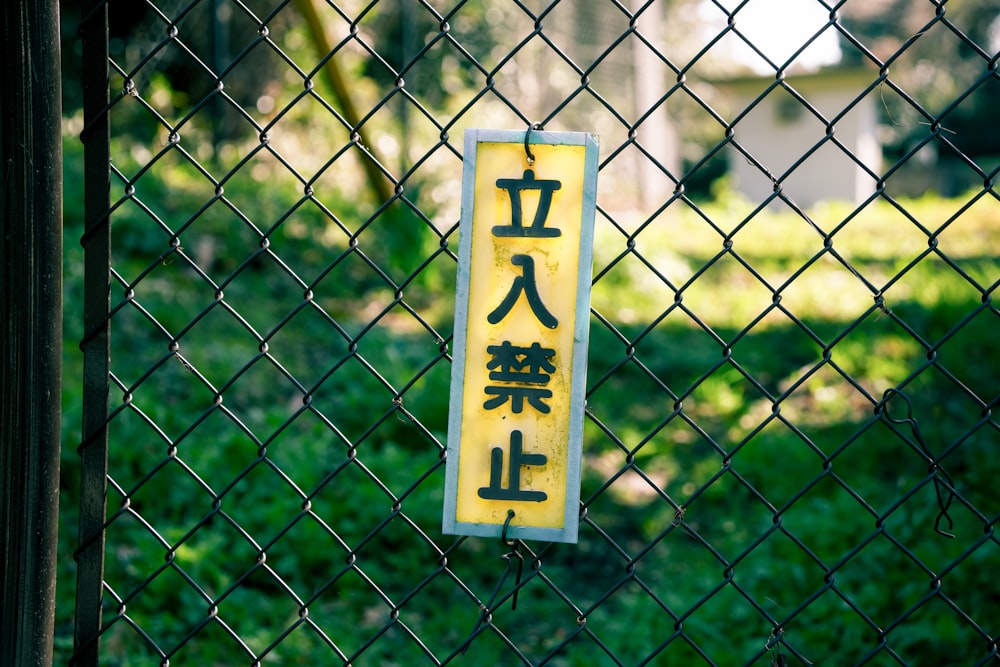 a yellow sign hanging on a chain link fence