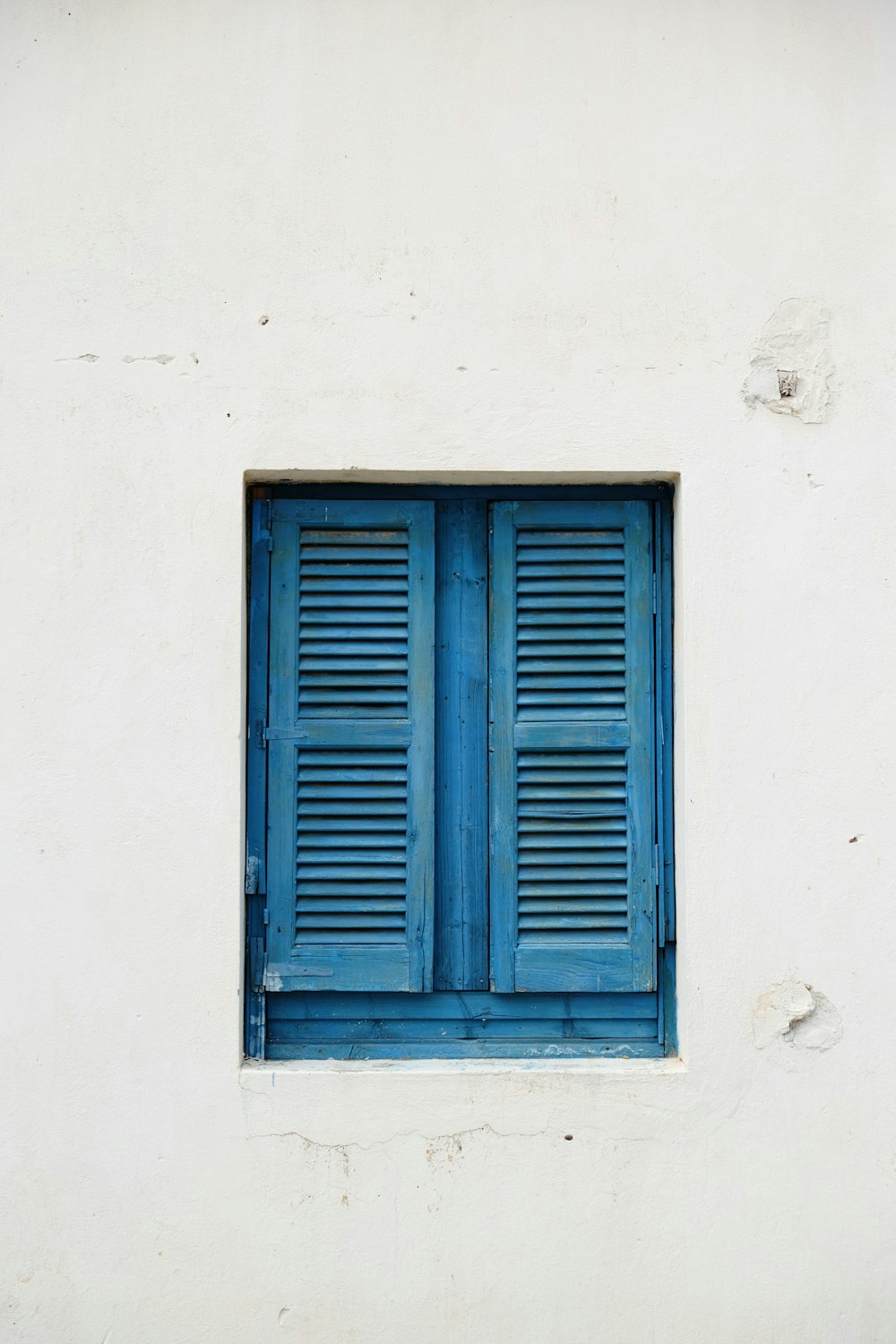 a blue window on a white wall with shutters