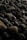 A close-up of a collection of smooth, dark-colored stones. The stones vary in size but share similar rounded shapes. Some of the stones have a slightly greenish hue while others are more brown or black. The lighting creates a subtle play of shadows and highlights on the surfaces of the stones.