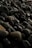 A close-up of a collection of smooth, dark-colored stones. The stones vary in size but share similar rounded shapes. Some of the stones have a slightly greenish hue while others are more brown or black. The lighting creates a subtle play of shadows and highlights on the surfaces of the stones.
