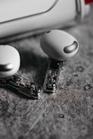 Two wireless earbuds with a sleek and modern design are lying on a textured gray surface. The earbuds feature a transparent section revealing internal components, adding a futuristic element to their appearance.
