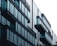 A modern building with a sleek, minimalist design featuring large glass windows and balconies extending from each floor. The structure appears symmetrical, with reflective surfaces that suggest a contemporary architectural style.