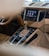 The interior view of a luxury car showing the gear shift, infotainment system screen with various icons for settings such as radio and phone, as well as the steering wheel. The dashboard and console have a sleek and modern design with a beige and black color scheme.