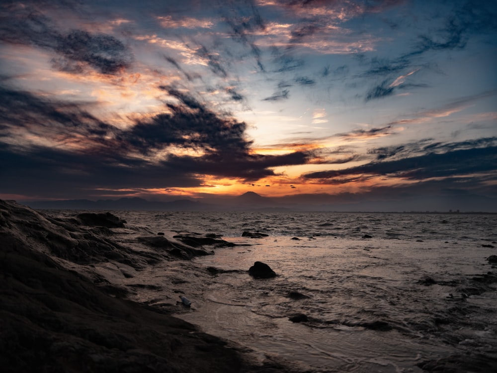 the sun is setting over the ocean on a cloudy day