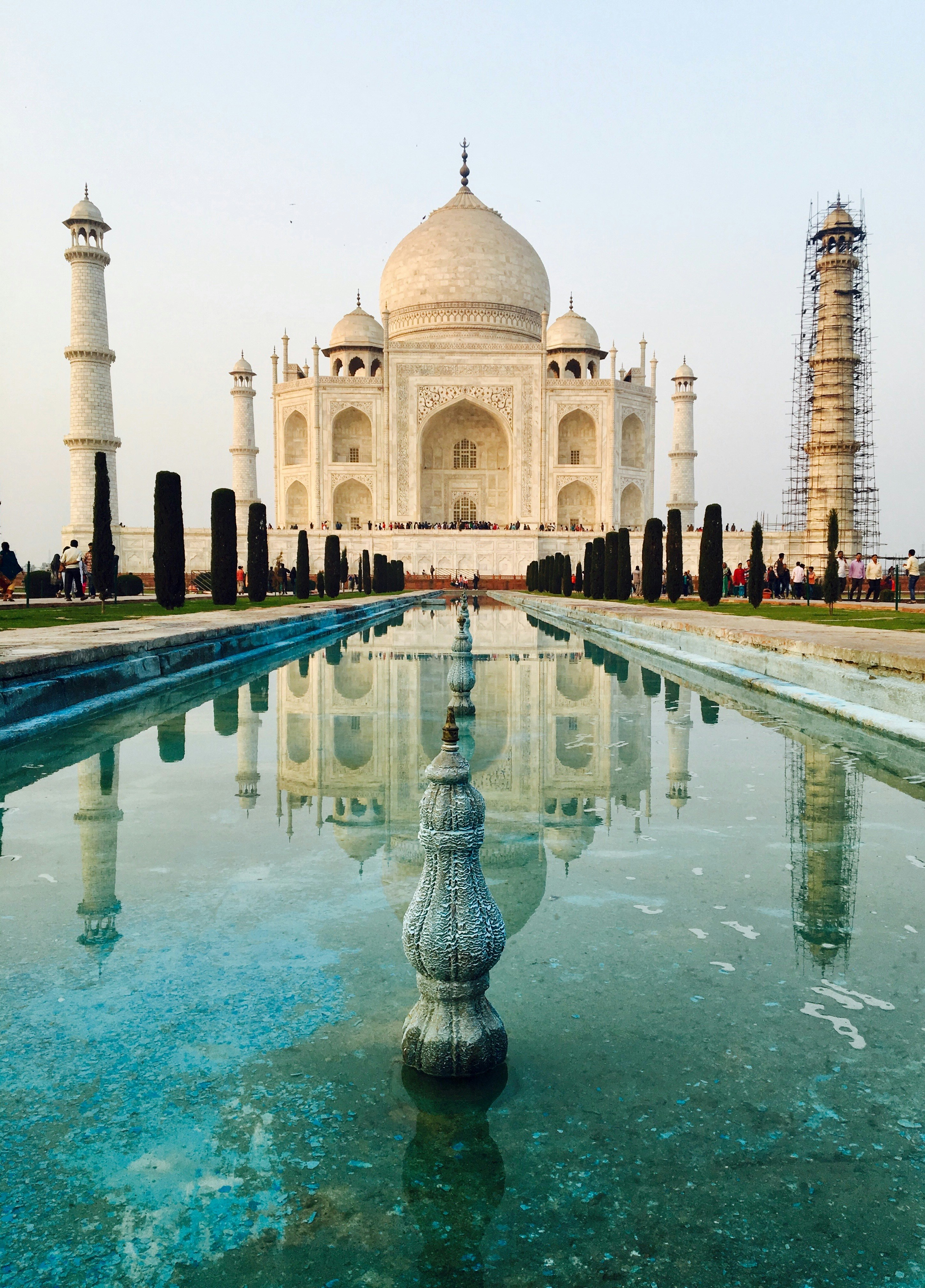 Taj Mahal at dawn bathed in soft pink light, white marble dome and minarets perfectly reflected in the long rectangular pool