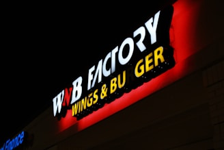 A brightly lit sign for a wings and burger restaurant, with bold white, red, and yellow letters against a dark background.