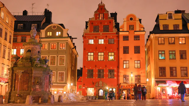 Stortorget, the main square of Gamla Stan, glowing at dusk with its colorful stepped-gable buildings and an old stone well in the foreground.
