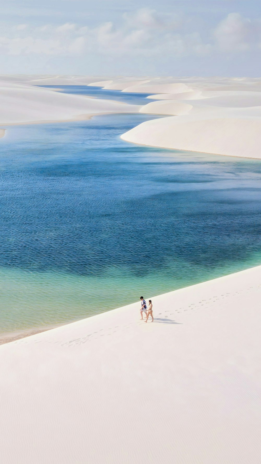 a couple of people walking across a sandy beach