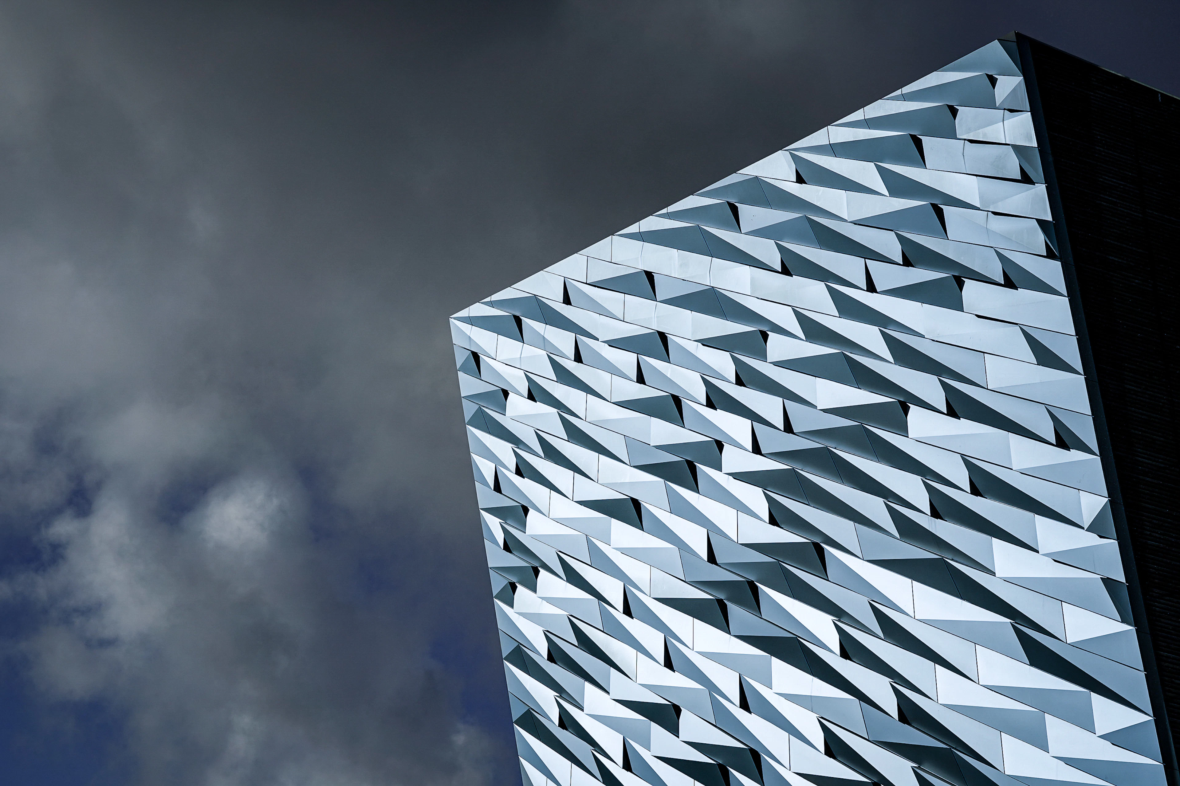 The angular silver-paneled facade of the Titanic Belfast museum against a dramatic cloudy sky.