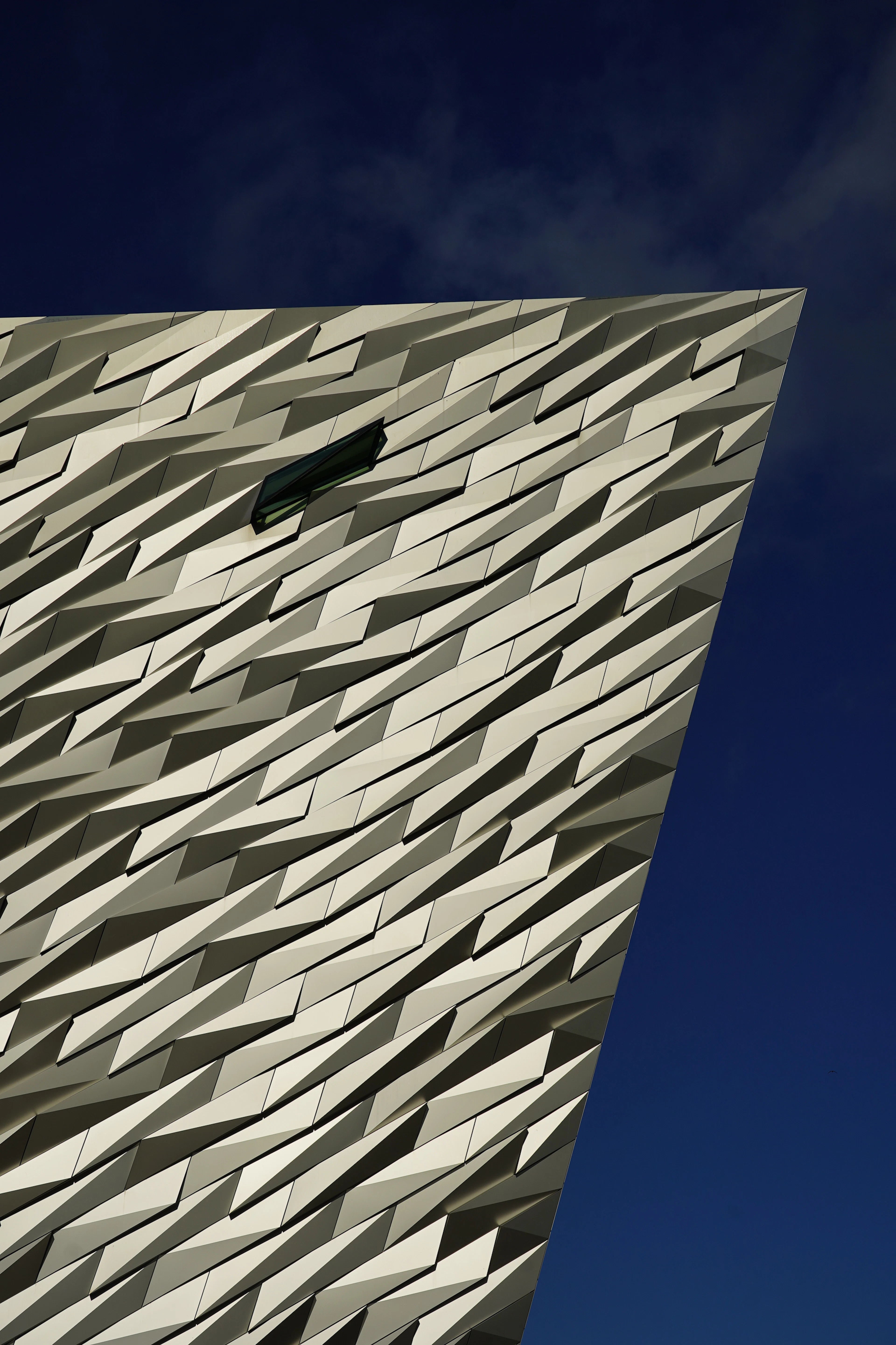 The angular silver aluminium facade of Titanic Belfast rising against a clear deep-blue sky.