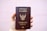 A hand is holding a brown passport with an emblem and text on the cover that indicates it is a Thailand passport. The text is in both Thai and English, and the background is plain and light-colored.