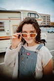 a woman in overalls holding up a pair of sunglasses