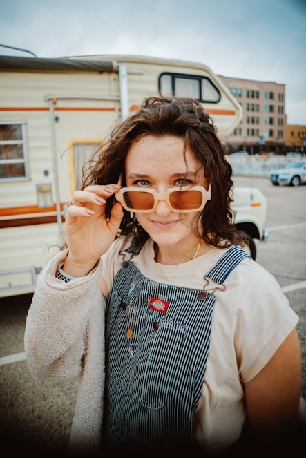a woman in overalls holding up a pair of sunglasses