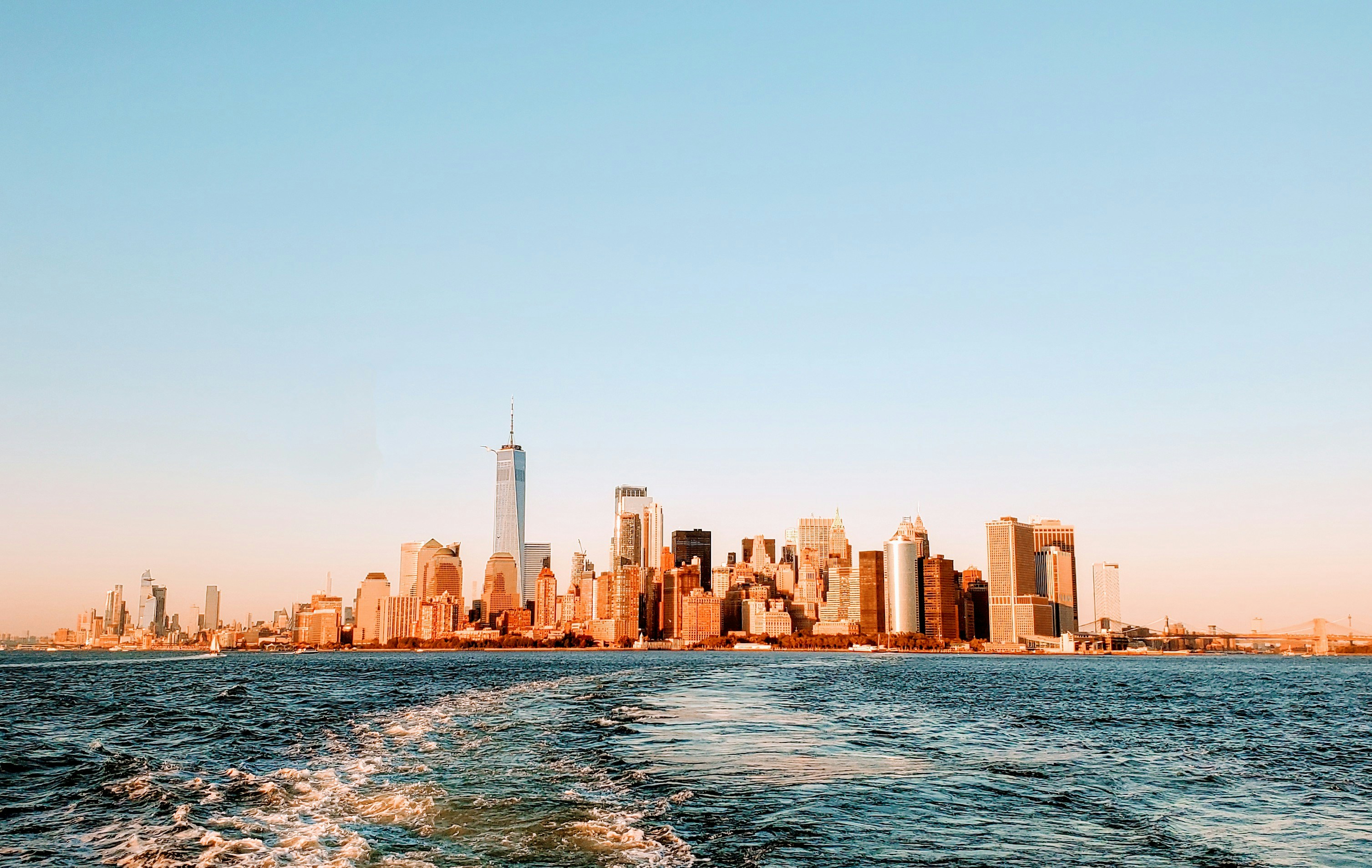 Skyline de Manhattan al atardecer visto desde el agua, edificios iluminados, Empire State Building prominente