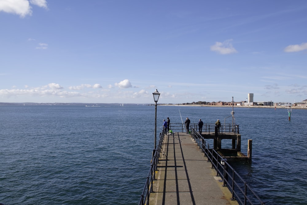 a pier with people standing on it next to the ocean