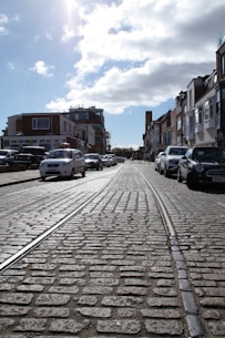 a cobblestone street with cars parked on both sides