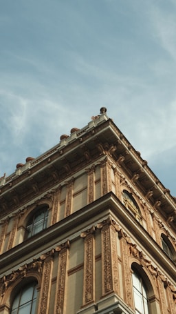 A well-preserved historic building with intricate architectural details. The facade features ornate carvings and decorative elements, characteristic of classical or Renaissance architecture. Large arched windows are symmetrically placed along the upper floors, and the building is topped with a balustrade.