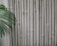A textured wall of vertical beige bamboo stalks is accompanied by lush green palm leaves extending from the left side. The surface of the bamboo is slightly rough, with natural variations and some nodes visible. The composition creates a natural and calming aesthetic.