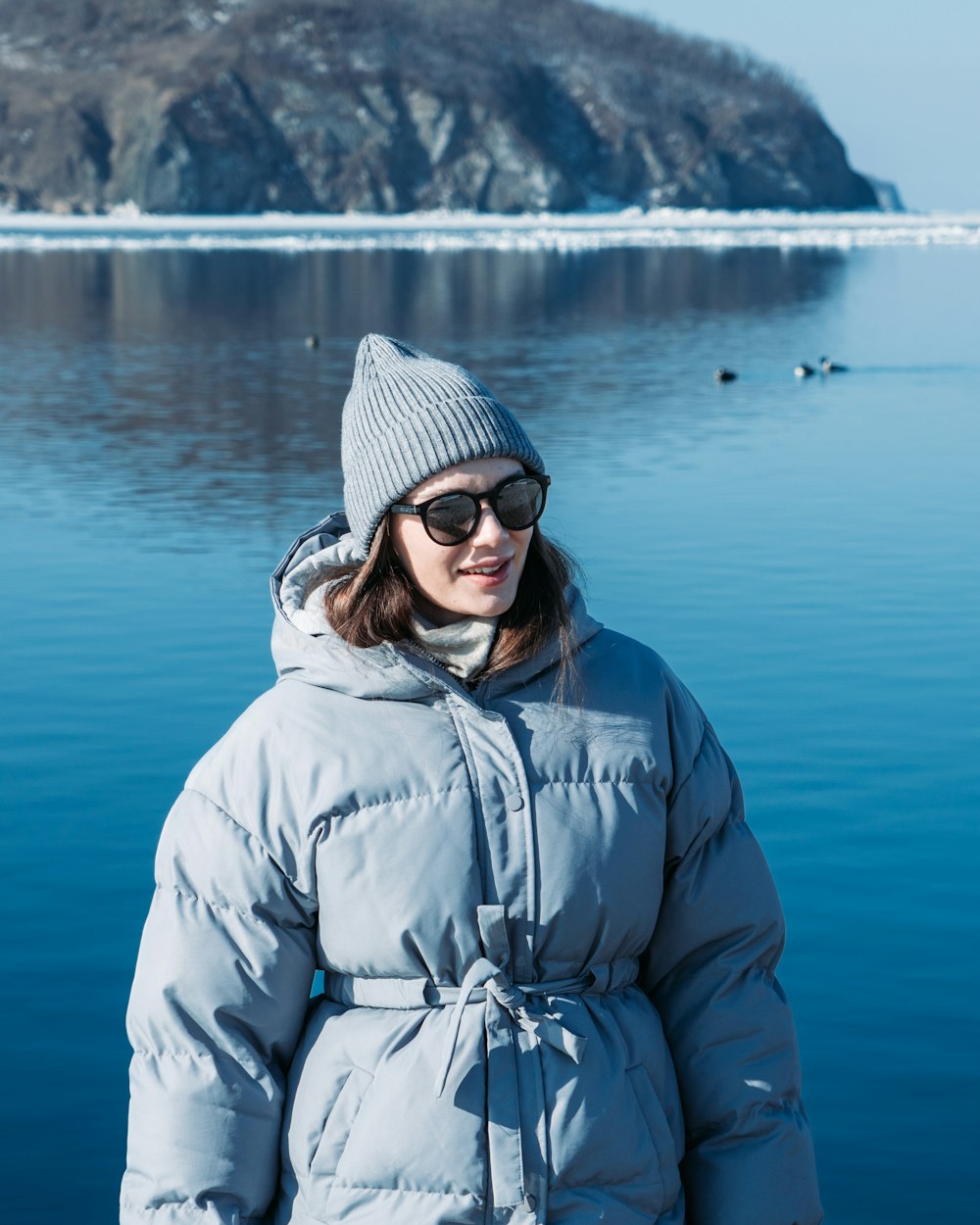 a woman in a blue coat and hat standing in front of a body of water